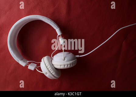Isolated modern white headphone over a red leather background. Stock Photo