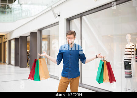 A photo of young man standing in the midle of the mall with shopping bags in his hands. He's smiling. Stock Photo