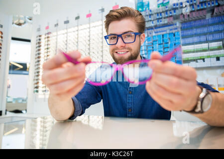 A photo of young, handsome man holding pink glassses in his hands. Stock Photo