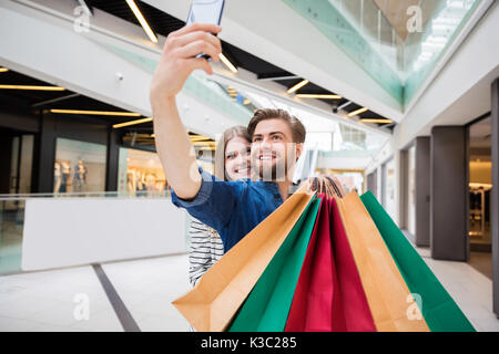 A photo of young, happy couple holding lots of shopping bags and taking themselves a photo. Stock Photo