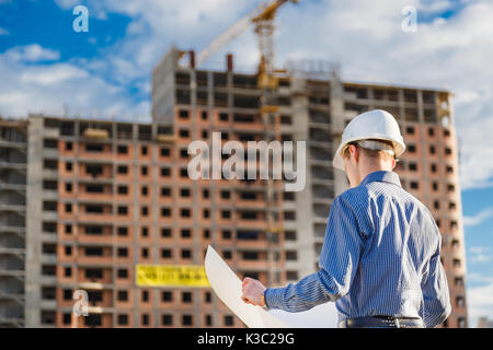 Architect in helmet with blueprints looks at camera in a building site Stock Photo
