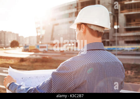 Architect in helmet with blueprints looks at camera in a building site Stock Photo