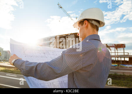 Architect in helmet with blueprints looks at camera in a building site Stock Photo