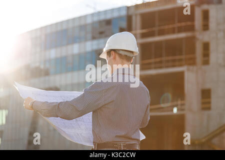 Architect in helmet with blueprints looks at camera in a building site Stock Photo