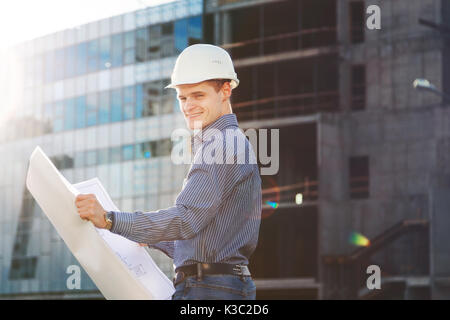 Architect in helmet with blueprints looks at camera at building site Stock Photo