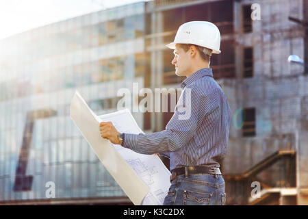 Architect in helmet with blueprints looks at camera in a building site Stock Photo