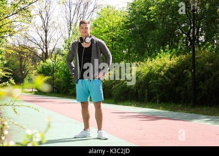 A photo of a young man in sports wear standing on the racetrack. Stock Photo