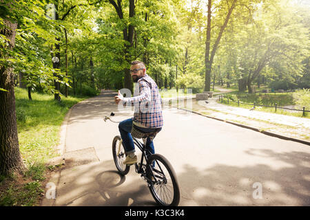 Portrait of young man riding bike in park showing thumb up Stock Photo