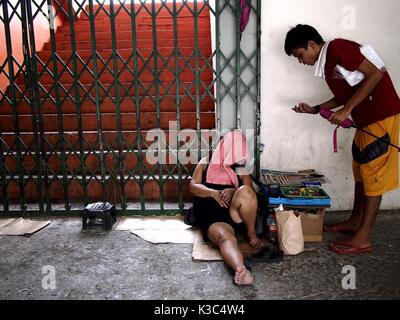 MARIKINA CITY, PHILIPPINES - AUGUST 28, 2017: A man tries to buy cigarette from a sleeping cigarette vendor outside a sports stadium in Marikina City. Stock Photo