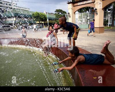 MARIKINA CITY, PHILIPPINES - AUGUST 28, 2017: Young children play and cool off at a water fountain at an outdoor park. Stock Photo