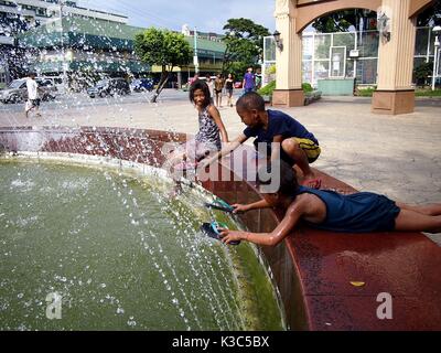 MARIKINA CITY, PHILIPPINES - AUGUST 28, 2017: Young children play and cool off at a water fountain at an outdoor park. Stock Photo