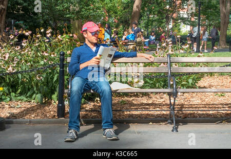 A young man reading the New Yorker Magazine and enjoying summer sunshine in Washington Square Park in Greenwich Village in NYC Stock Photo