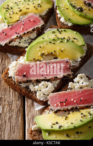 sandwiches with fillet of tuna, avocado and cream cheese close-up on table. vertical Stock Photo