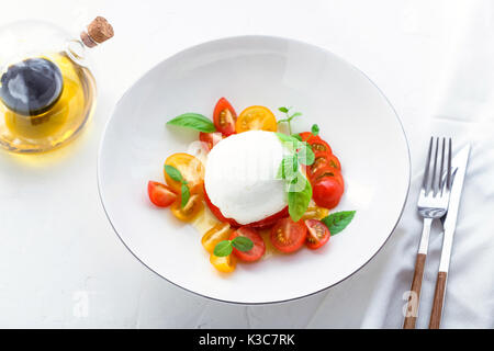Italian appetizer caprese salad with ripe red and yellow cherry tomatoes, mozarella, fresh basil leaves and olive oil. White background. Stock Photo