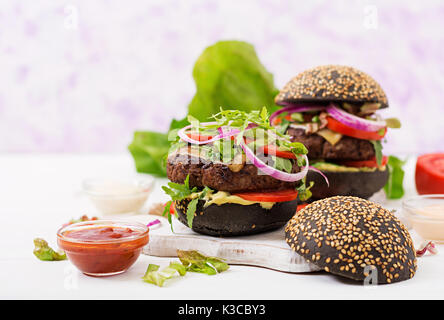 Black big sandwich -  black hamburger with juicy beef burger, cheese, tomato,  and red onion on light background. Stock Photo