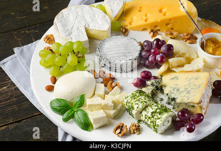 Cheese plates served with grapes, jam,  and nuts on a wooden board.Top view Stock Photo