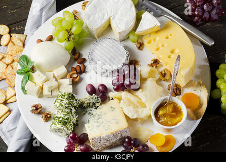 Cheese plates served with grapes, jam,  and nuts on a wooden board.Top view Stock Photo