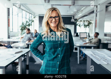 Attractive businesswoman in casuals at modern office. Caucasian female smiling with colleagues working in background. Stock Photo