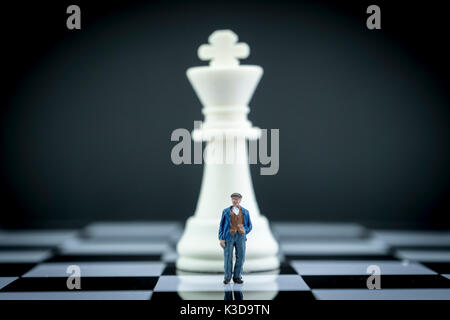 Miniature figure of a man in front of chess piece, conceptual image