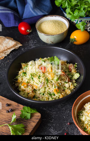 Lebanese arabic cuisine: healthy delicious salad with cous cous, fresh vegetables and greens called Tabbouleh in black bowl. Authentic cuisine Stock Photo