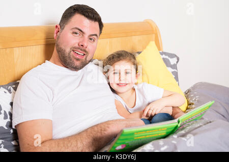 Happy father reading a story to his daughter in a bedroom Stock Photo