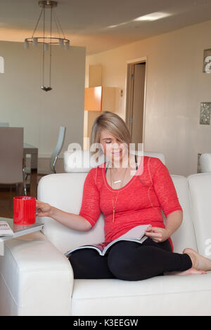 A happy woman sitting on a sofa reading a book. Stock Photo