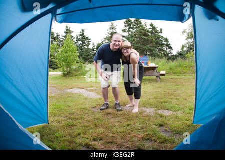 a young couple framed by their camping tent smiling and enjoying the outdoors Stock Photo