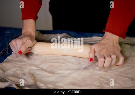 master shapes pottery on a blue canvas.Creative process. Gives shape to your product.Spread the clay with a rolling pin Stock Photo