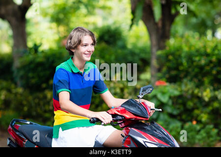 Teenager riding scooter. Teenage boy fun on motorbike ride on his way to school. Student on motorcycle in tropical city. Transportation and travel for Stock Photo