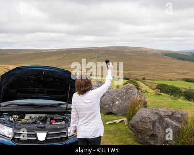 Mature, senior, attractive lady stranded in countryside with broken down care trying to get a cell phone signal to call for help. Stock Photo