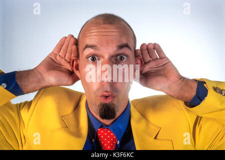 Man in a yellow sports jacket holds hands to the ears Stock Photo