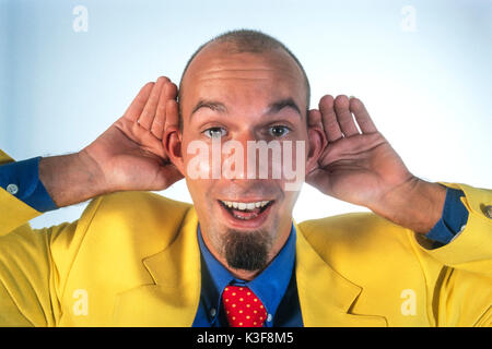 Man in a yellow sports jacket holds hands to the ears Stock Photo