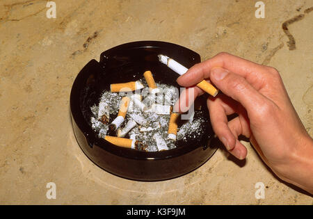 Smoker close burning cigarette in the hand and ashtray Stock Photo