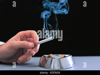 Smoker close burning cigarette in the hand and ashtray Stock Photo