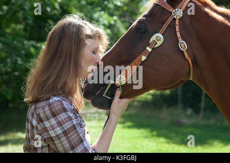 Side view of woman kissing muzzle of brown horse. Stock Photo
