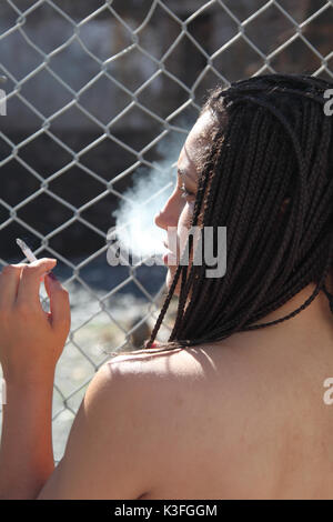 black woman metal fence smoking Stock Photo
