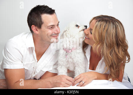 Happy couple with young pet dog, puppy kissing woman. Stock Photo