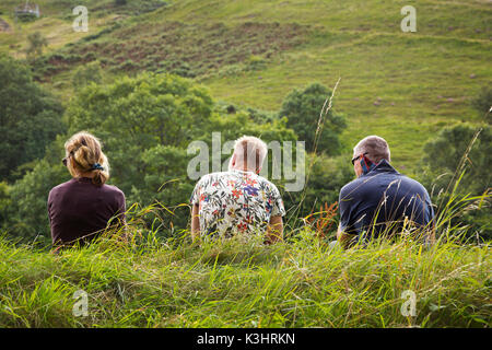 Three people sitting on a grassy  bank Stock Photo
