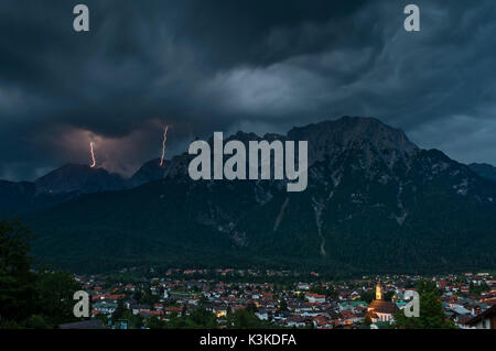 Lightning strike in northern Karwendelgebirge (mountains) over the violin maker village Mittenwald. Dramatic beautyful clouds and enlightened church. Stock Photo