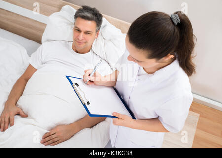 Female Doctor Writing On Clipboard Standing Near Patient Stock Photo