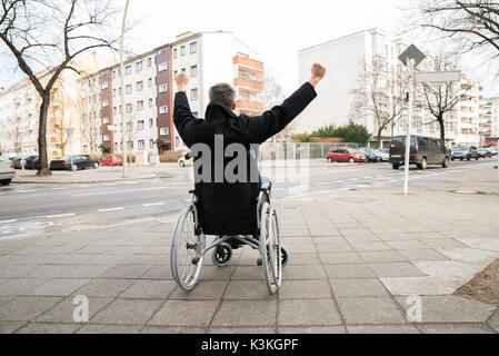 Rear View Of A Disabled Man On Wheelchair With Hand Raised Stock Photo