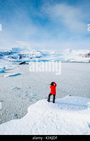 Fjallsarlon glacier lagoon, East Iceland, Iceland. Man with red coat admiring the view of the frozen lagoon in winter (MR). Stock Photo