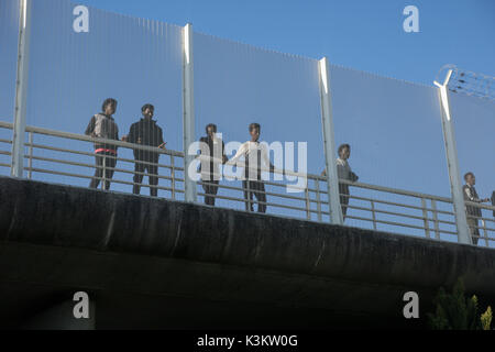 Refugees watch the traffic on the approach road from a bridge behind a high fence. Refugees are back in Calais, nearly a year after the refugee camp known as The Jungle was dismantled by the French State and the refugees were being sent to reception centres all over France. The refugees are still trying to reach the UK. One way they are trying is to enter trucks on the Route national 216, the approach road that leads to the port of Calais and the ferries going to the UK, when the traffic has stopped on the road. (Photo by Michael Debets/Pacific Press) Stock Photo