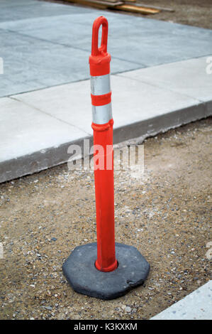 A safety cone standing between the gap betweem the driveway and the road. Stock Photo