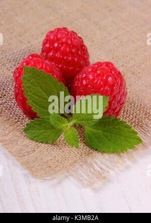 Fresh ripe raspberries and leaf of lemon balm on jute canvas, concept of healthy food and dessert Stock Photo