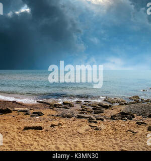 seascape image of sandy and rocky beach over stormy sky Stock Photo