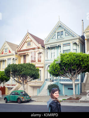 A girl and green Volkswagen Beetle in front of the 'Painted Ladies' row of Victorian Houses on Steiner Street (at Alamo Square) in San Francisco. Stock Photo