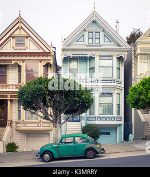 A green Volkswagen Beetle parked in front of the 'Painted Ladies' row of Victorian Houses on Steiner Street (at Alamo Square) in San Francisco. Stock Photo