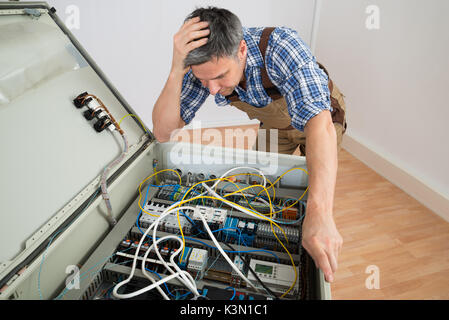 Portrait Of A Confused Electrician Looking At Fuse Box Stock Photo