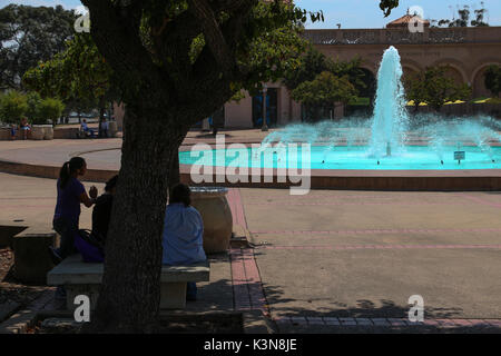 Silhouetted family resting under tree near the Bea Evenson fountain on the Plaza de Balboa, opposite the Reuben H. Fleet Science Museum, Balboa Park. Stock Photo